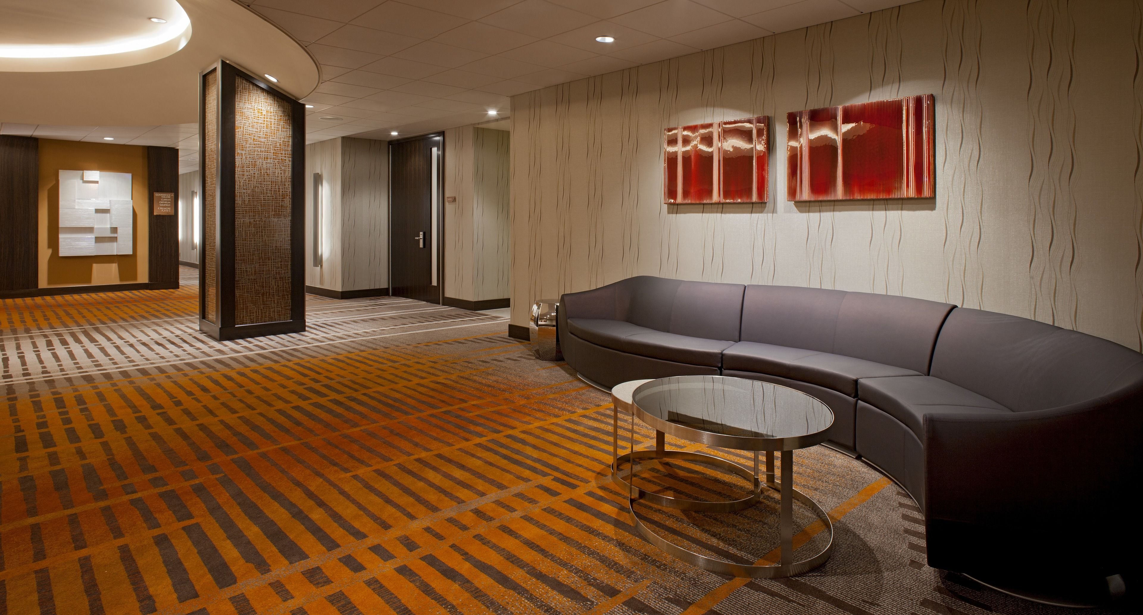 A modern lobby with a patterned carpet, a sofa, a glass coffee table, and two wall-mounted red panels.