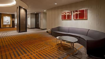 A modern lobby with a patterned carpet, a sofa, a glass coffee table, and two wall-mounted red panels.