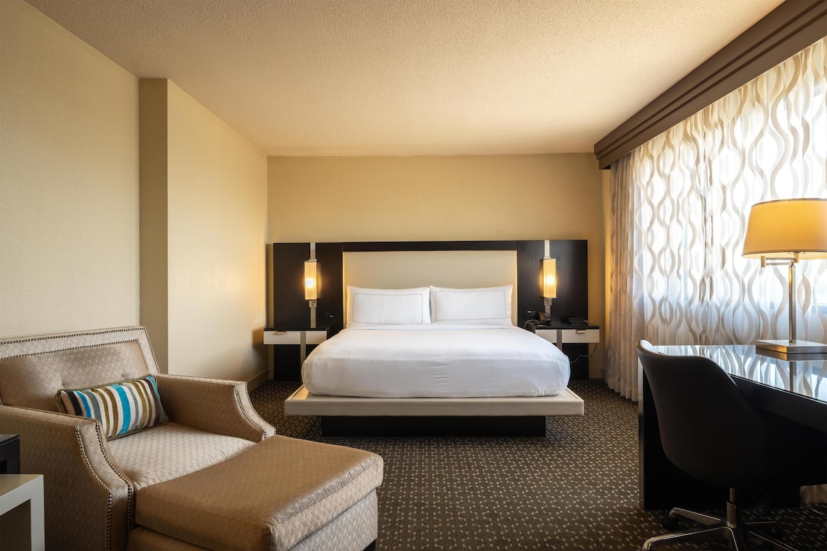 A hotel room with a large bed, a desk, a chair, and two bedside lamps.