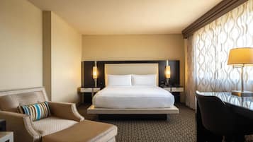 A hotel room with a large bed, a desk, a chair, and two bedside lamps.