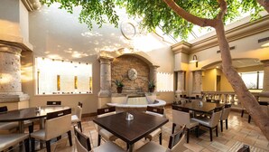 A dining area with multiple tables and chairs, a stone fireplace, and a large window. - Doubletree by Hilton Houston Hobby Airport (Houston)