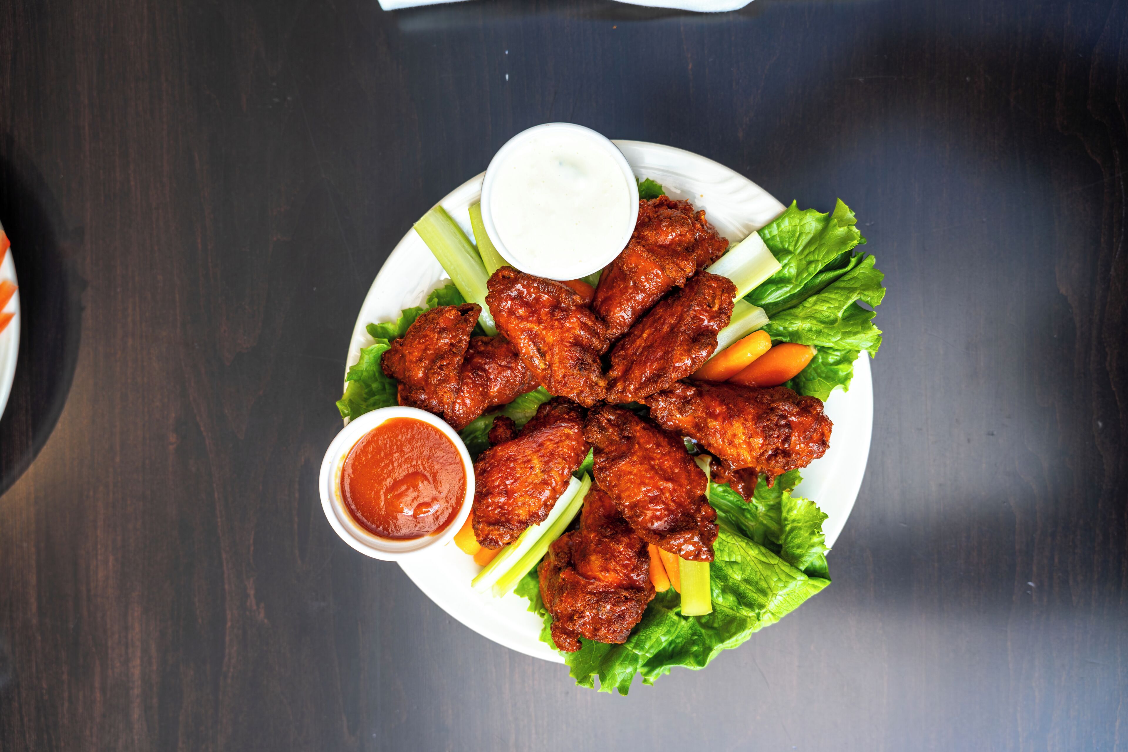 A plate of chicken wings with celery and carrots, and two dipping sauces.