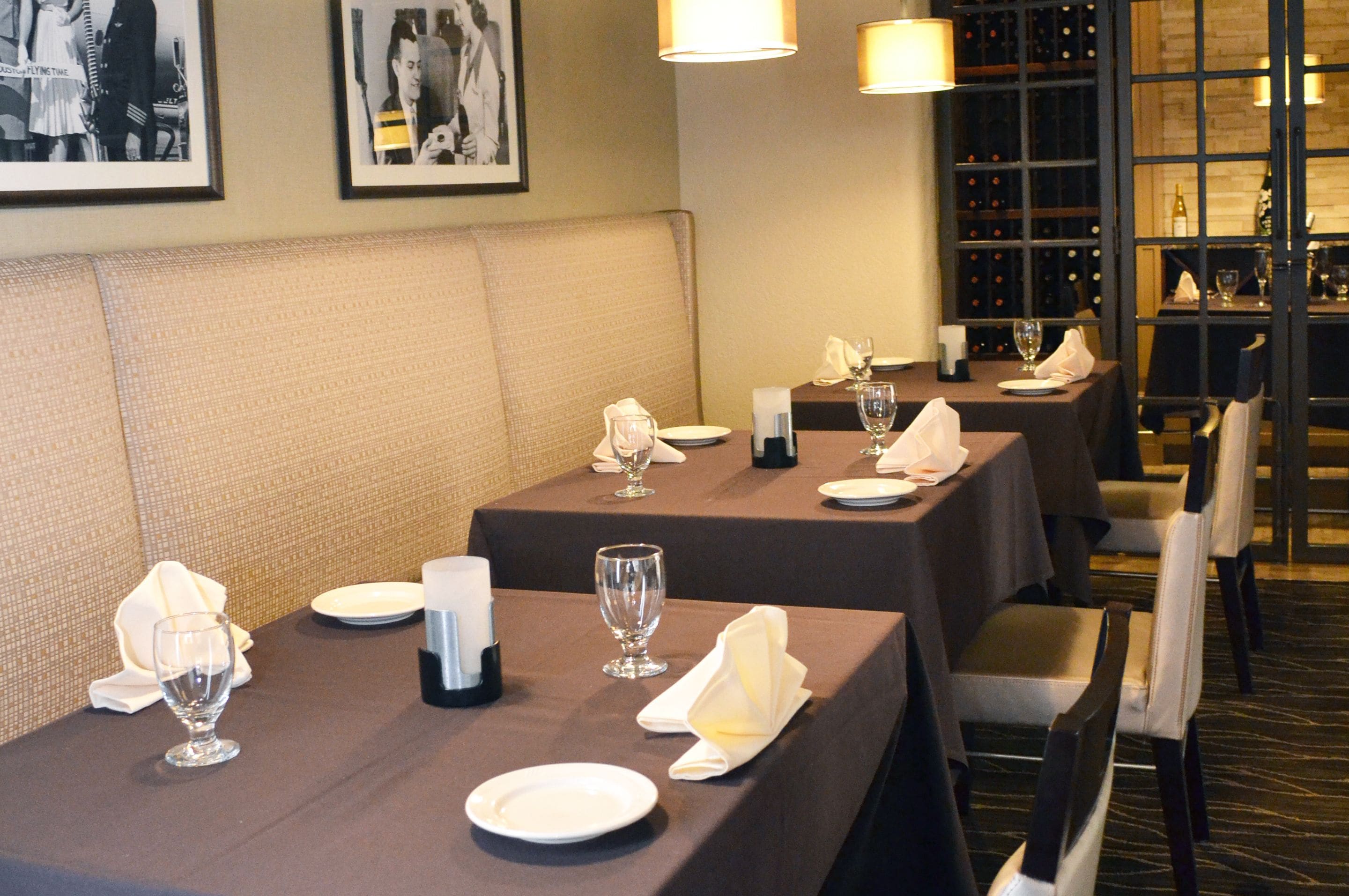 Un restaurante con mesas dispuestas para comer, con cabinas acolchadas y una estantería de vinos al fondo.