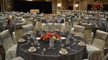 Un salón de banquetes con mesas redondas dispuestas para un evento formal, cada una con loza, cubiertos y centros de mesa florales.