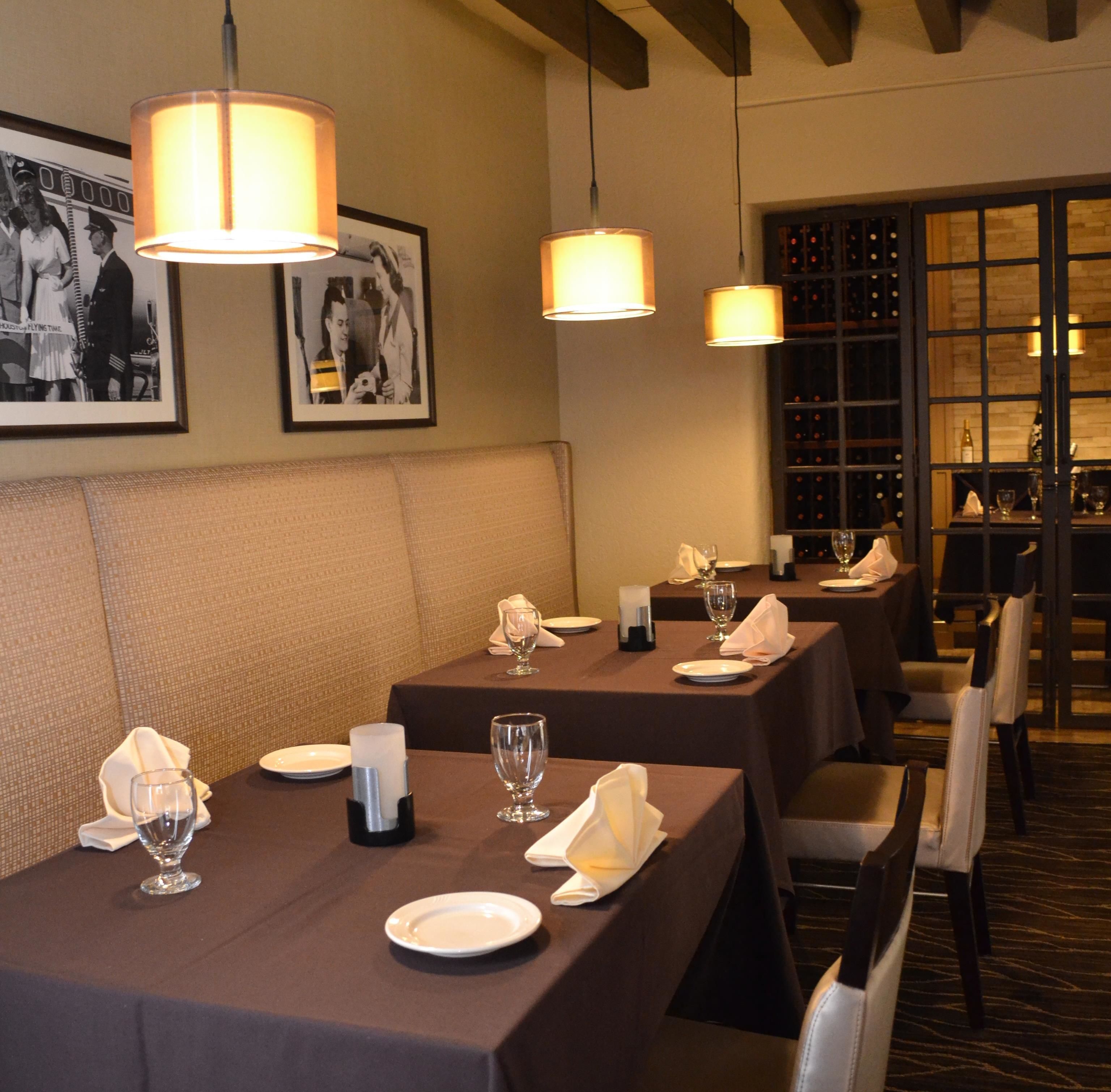 A restaurant with tables set for dining, framed pictures on the wall, and a wine rack in the background.