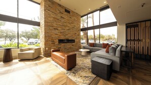 A modern living room with a stone fireplace, large windows, and a mix of seating arrangements. - Doubletree by Hilton Houston Hobby Airport (Houston)