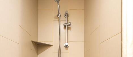A small, tiled shower stall with a handheld showerhead, a grab bar, and a safety bar on the floor.