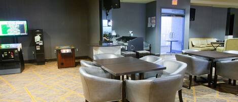 A hotel lobby with a reception desk, a TV, a bar area, and seating arrangements.