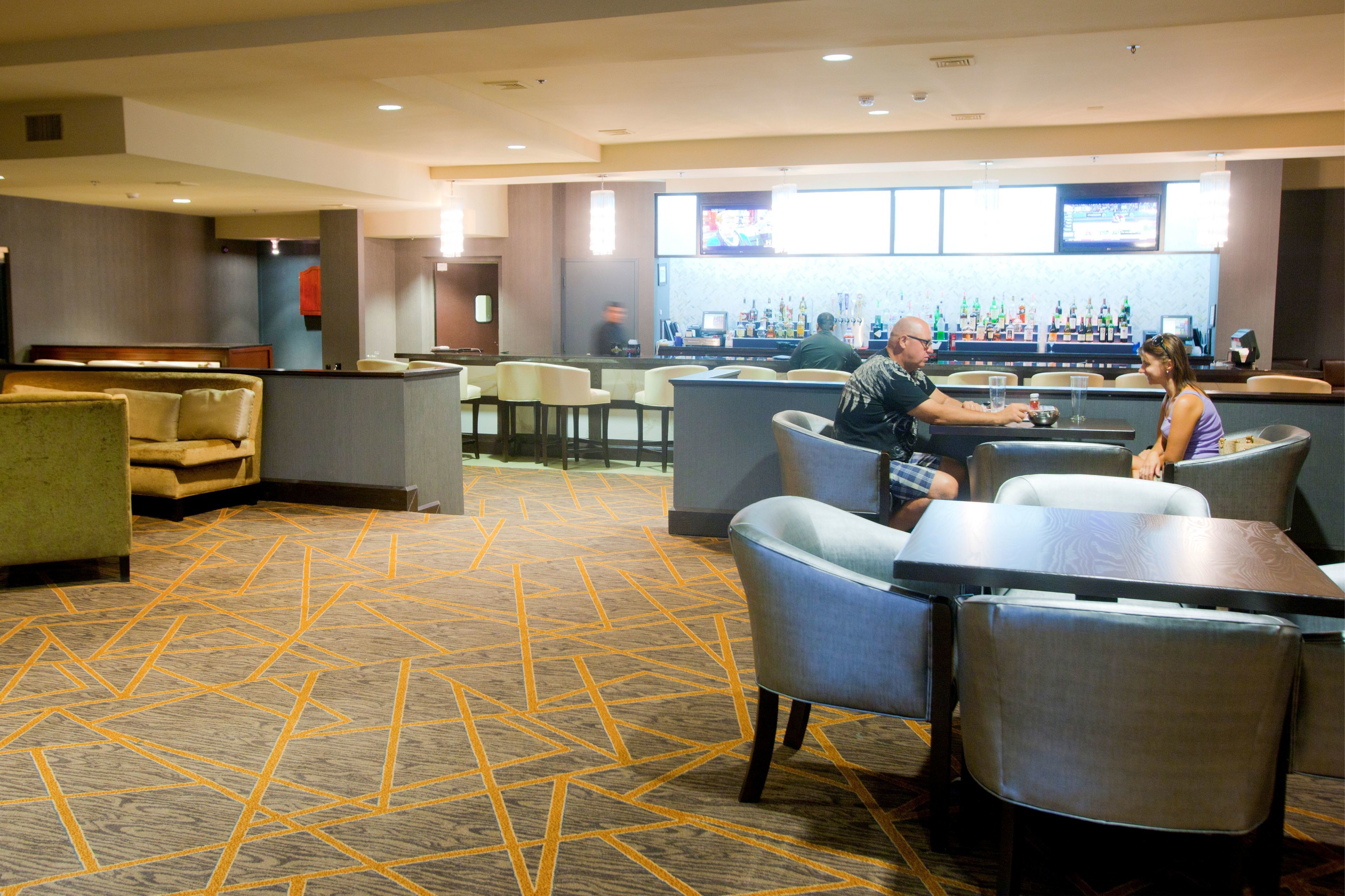 A hotel lobby with seating areas, a bar, and a television screen.