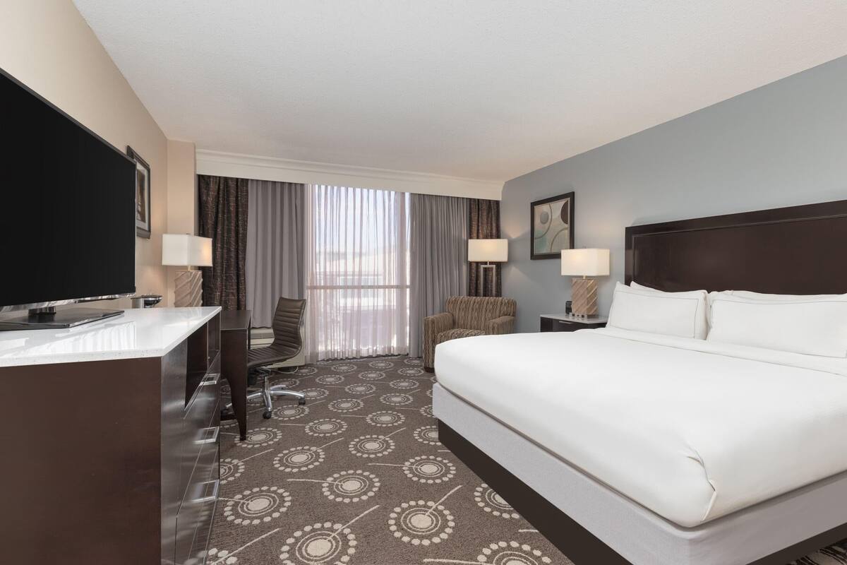 A hotel room with a large bed, a desk, a chair, and a television.