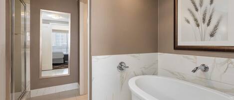 A modern bathroom with a freestanding bathtub, marble walls, and a framed plant.