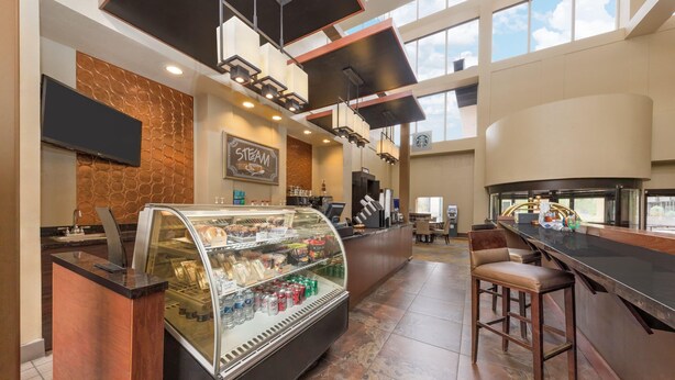 A modern coffee shop with a glass display case filled with pastries and beverages, a coffee machine, and a seating area with bar stools. - Wyndham Midland Downtown (Midland)
