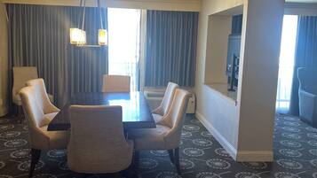 A hotel room with a dining area featuring a table and four chairs, a chandelier, and a large window with curtains.