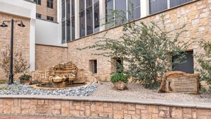 A courtyard with a stone fountain, a plaque, and a building with large windows. - Wyndham Midland Downtown (Midland)