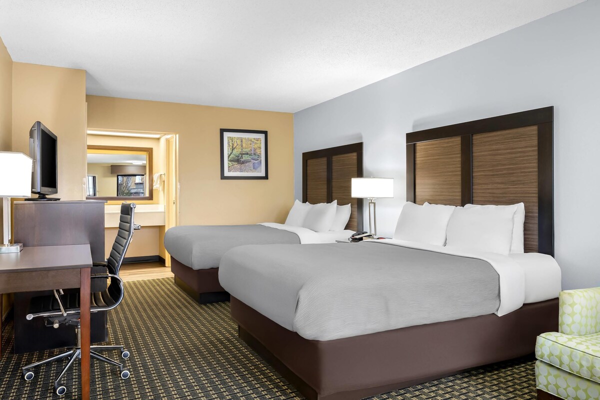A hotel room with two beds, a desk with a computer, a chair, and a small table.
