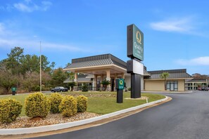 A hotel entrance with a sign reading "Quality in by Marriott" and a parking area with a few cars.