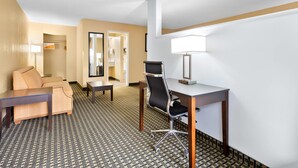 A hotel room with a sofa, a desk, a chair, a lamp, and a patterned carpet. - Quality Inn Perry - National Fairgrounds Area (Perry)