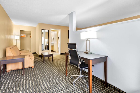 A hotel room with a sofa, a desk, a chair, a lamp, and a patterned carpet.