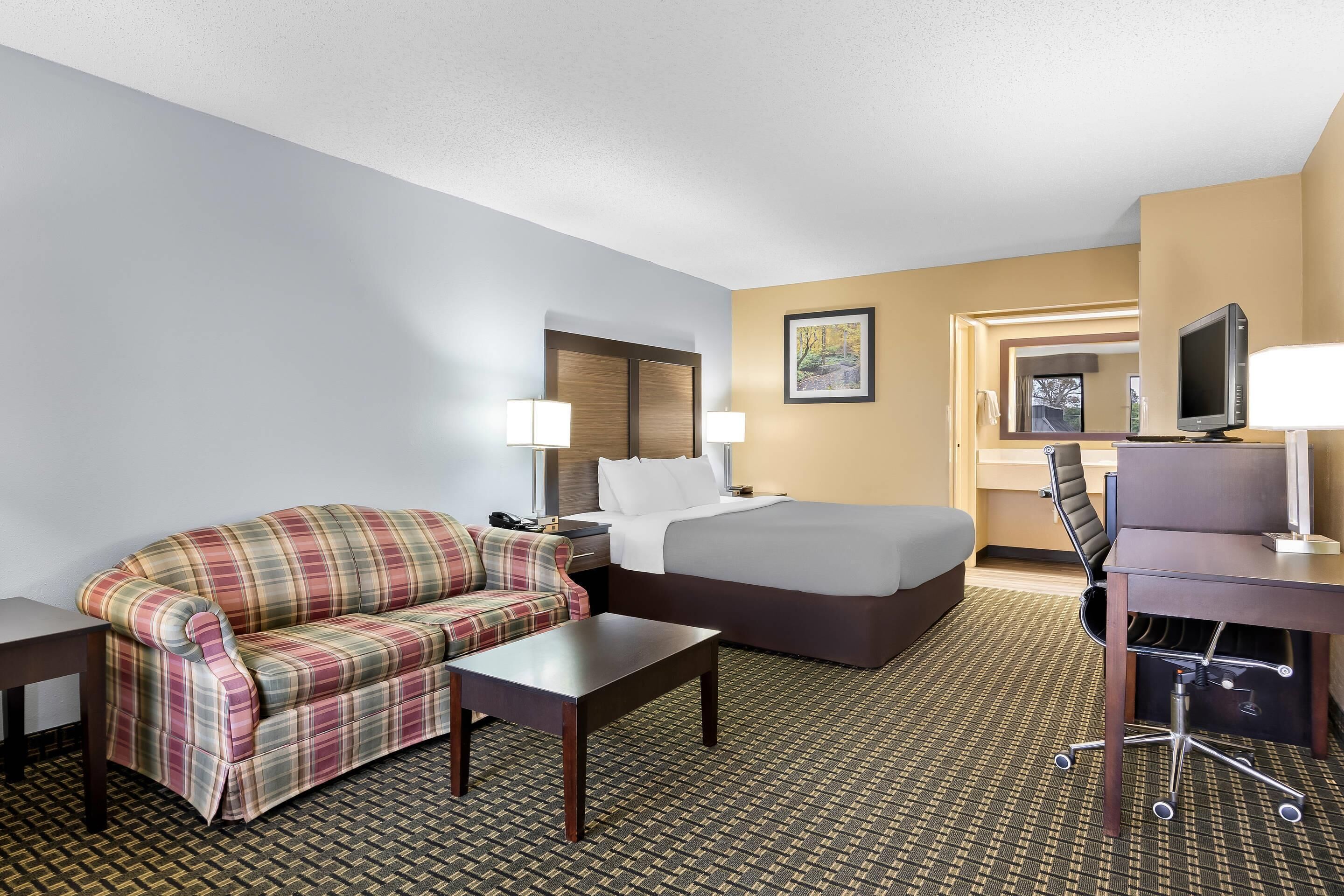 A hotel room with a plaid sofa, a bed, a desk with a chair, and a television.
