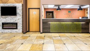 A hotel reception area with a stone fireplace, a flat-screen TV, and a reception desk with a green accent wall. - Quality Inn Perry - National Fairgrounds Area (Perry)