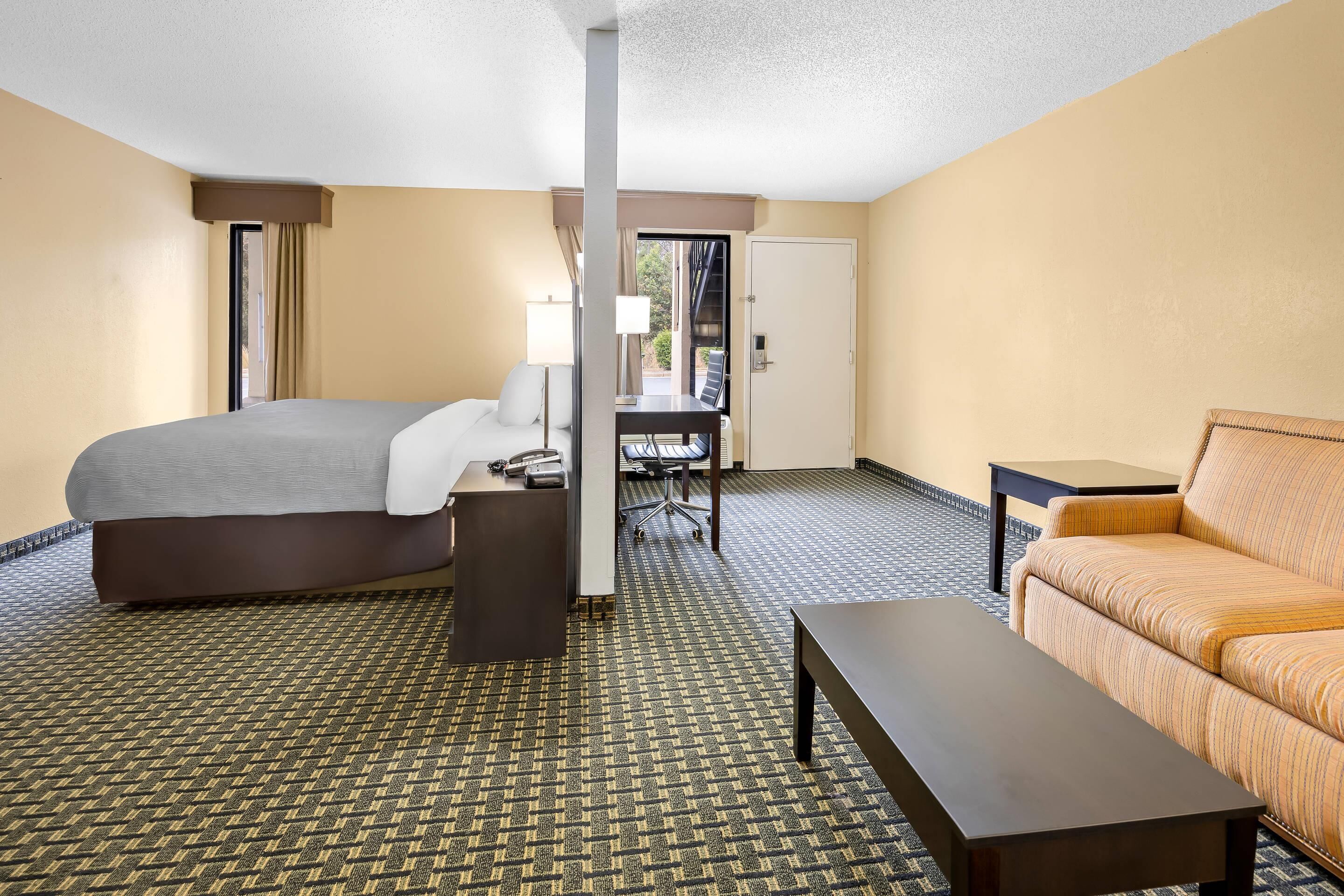 A hotel room with a bed, a desk, a chair, a sofa, and a small table.