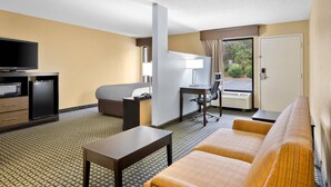 A hotel room with a sofa, a desk, a television, and a minibar. - Quality Inn Perry - National Fairgrounds Area (Perry)