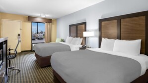 A hotel room with two beds, a desk, a chair, a lamp, and a view of the parking lot. - Quality Inn Perry - National Fairgrounds Area (Perry)