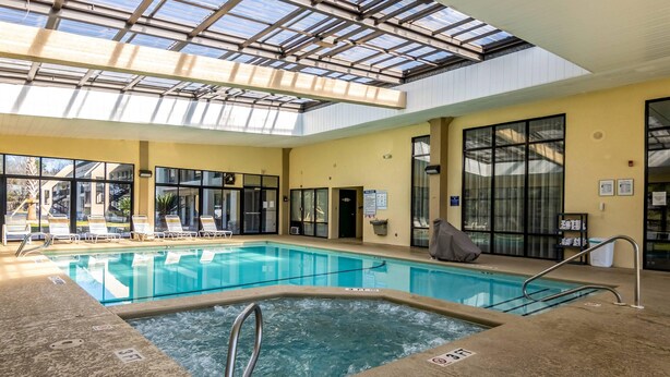 An indoor swimming pool with a skylight, clear glass walls, and a poolside area with lounge chairs. - Quality Inn Perry - National Fairgrounds Area (Perry)