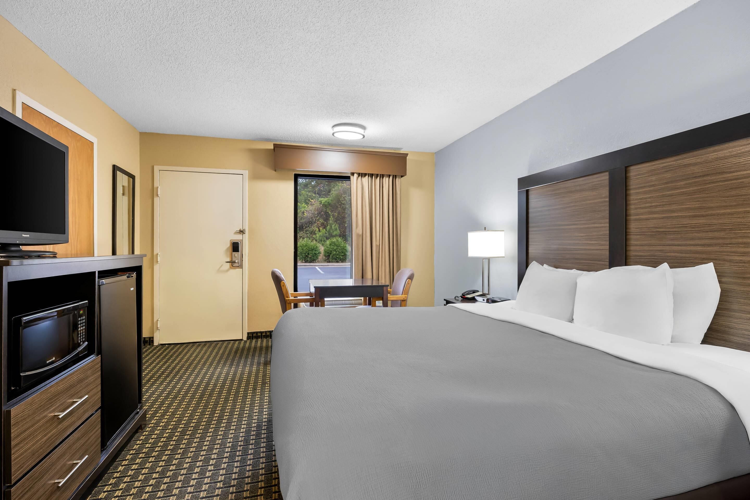 A hotel room with a large bed, a desk with a chair, a television, and a minibar.