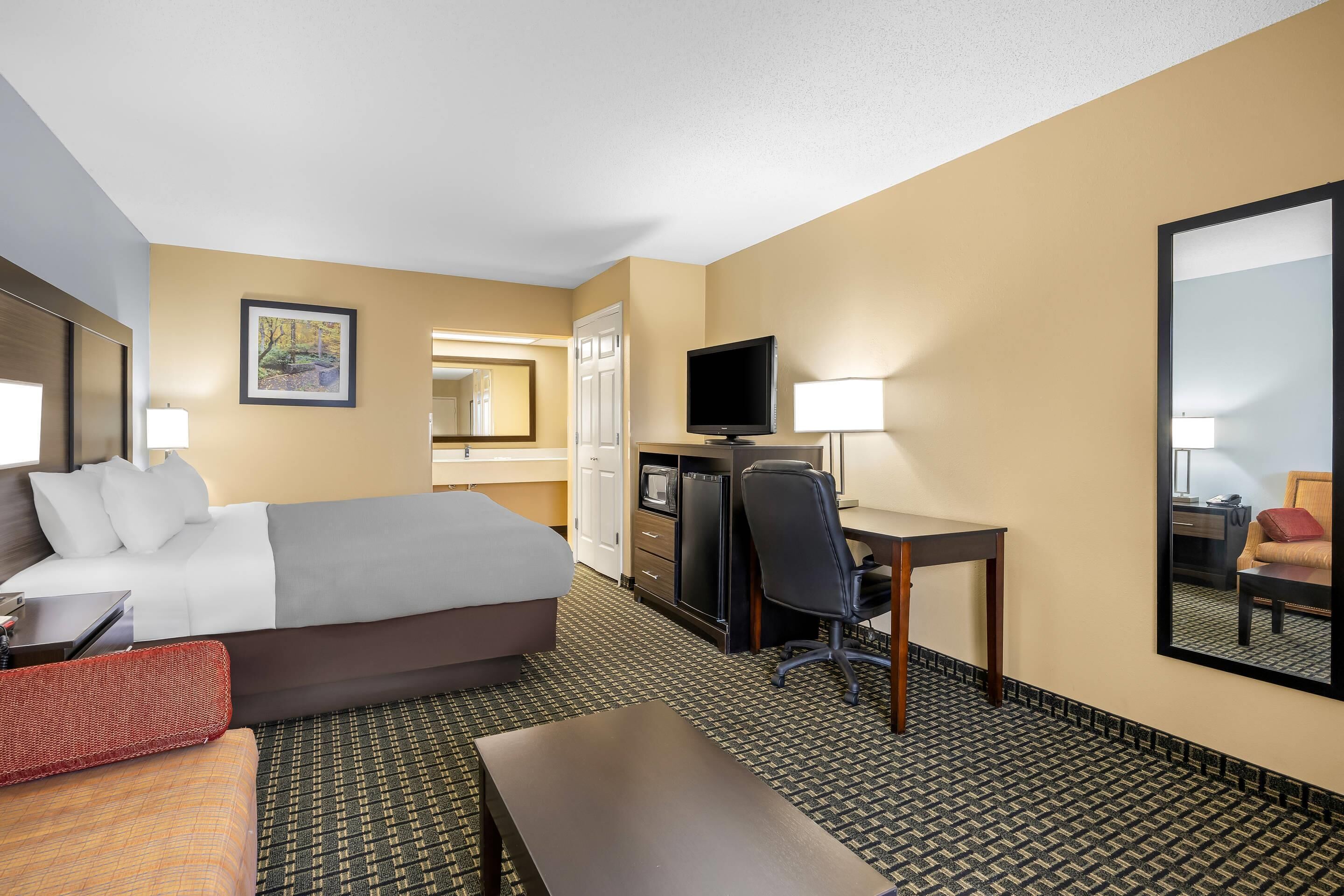A hotel room with a bed, desk, chair, and a television.