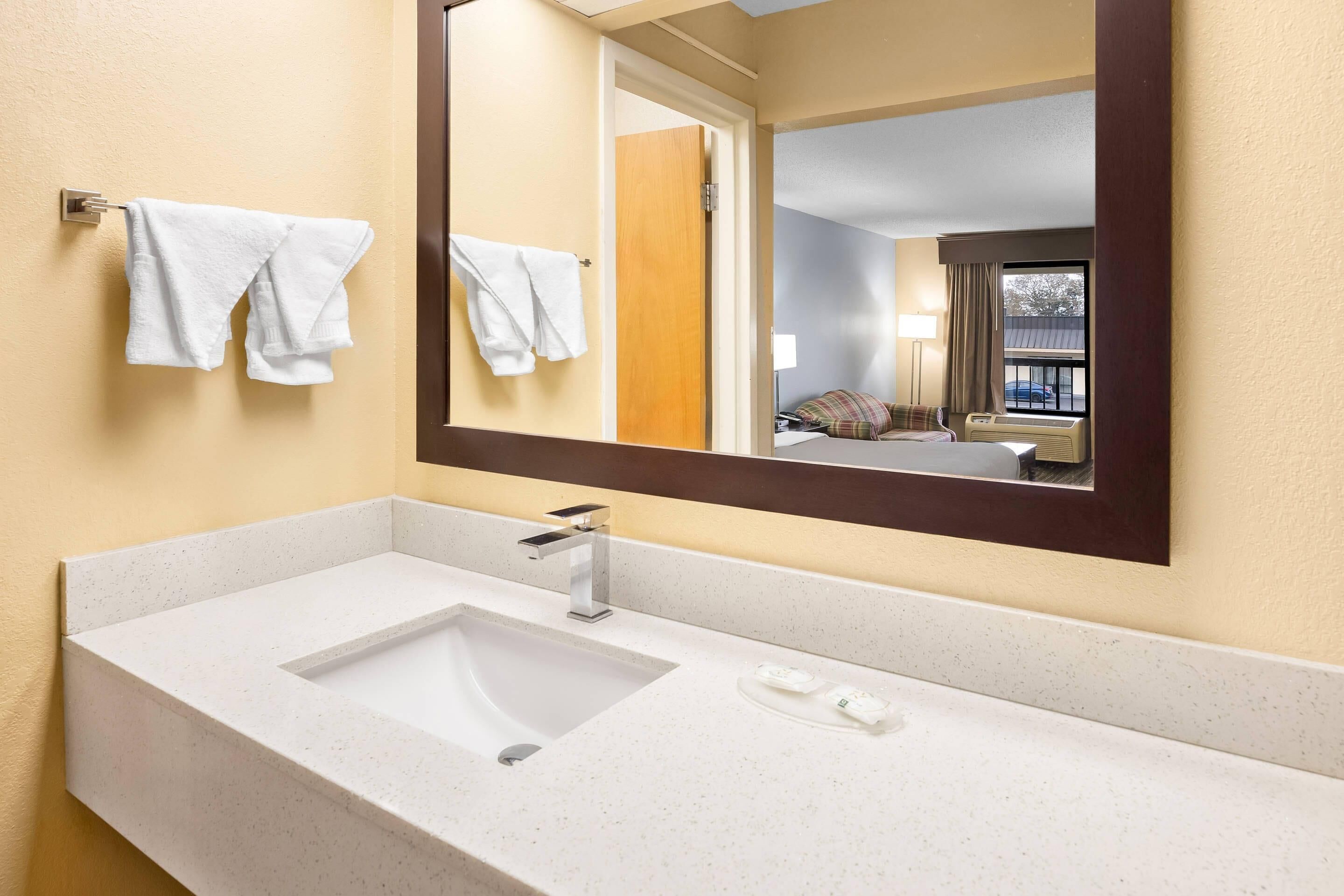 A hotel bathroom with a white sink, a mirror, and towels on a rack.