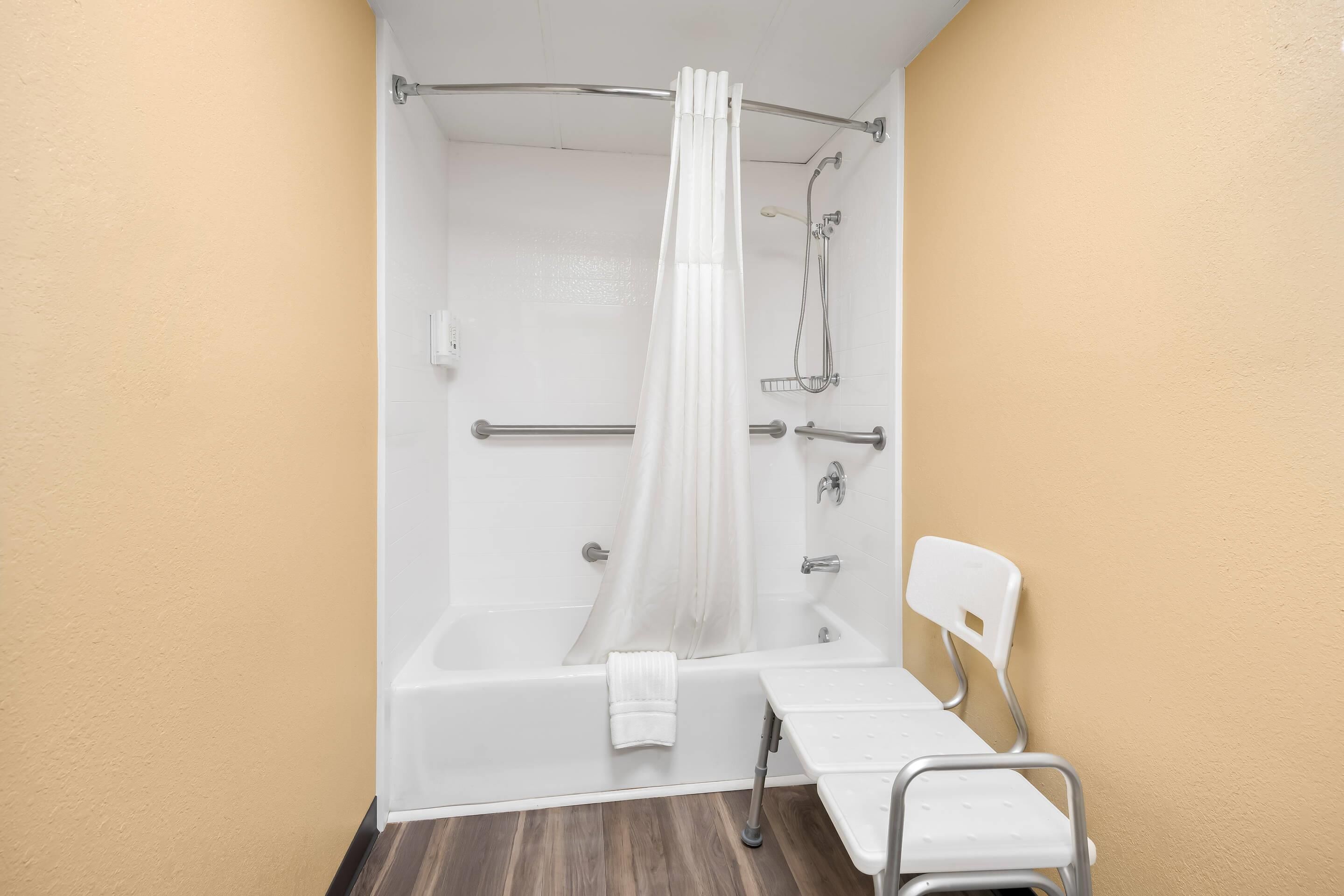 Une salle de bain avec une baignoire, une douche, une chaise blanche et un porte-serviettes.