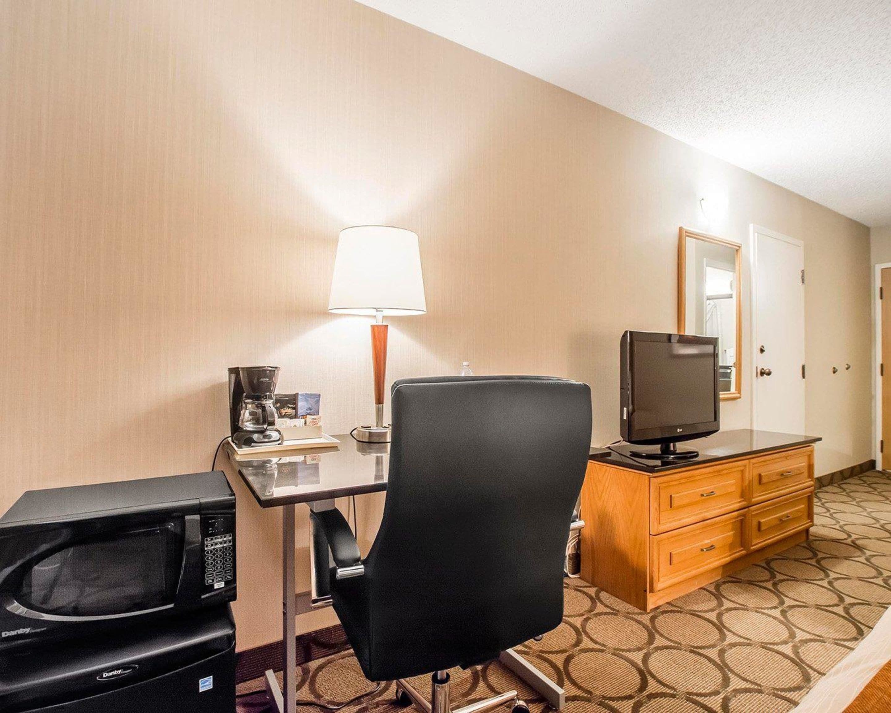 Habitación de hotel con escritorio, silla, televisor, microondas, lámpara y cómoda.