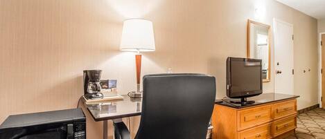 Habitación de hotel con escritorio, silla, televisor, microondas, lámpara y cómoda.