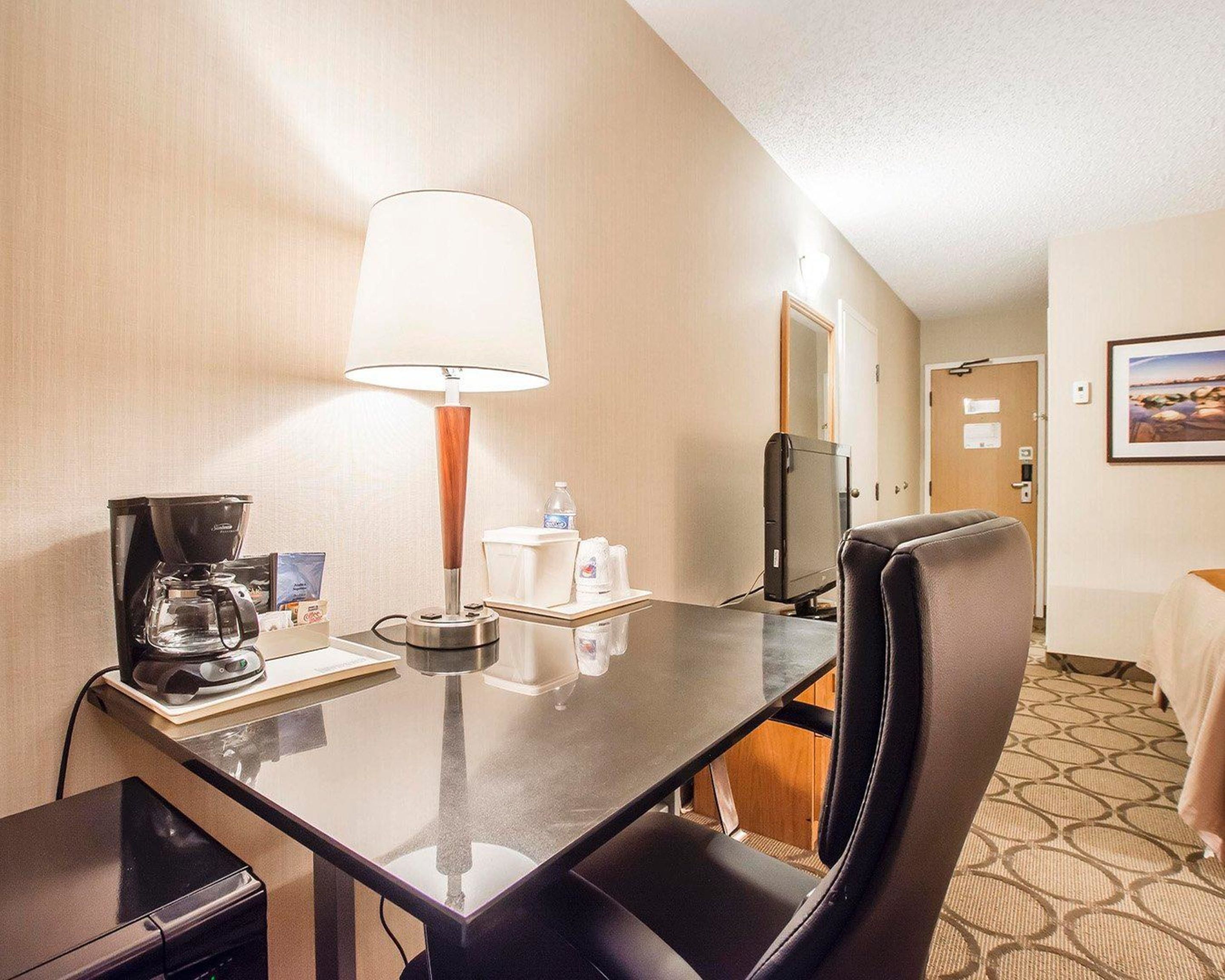 A hotel room with a dining table, a coffee maker, a lamp, a TV, and a bed.