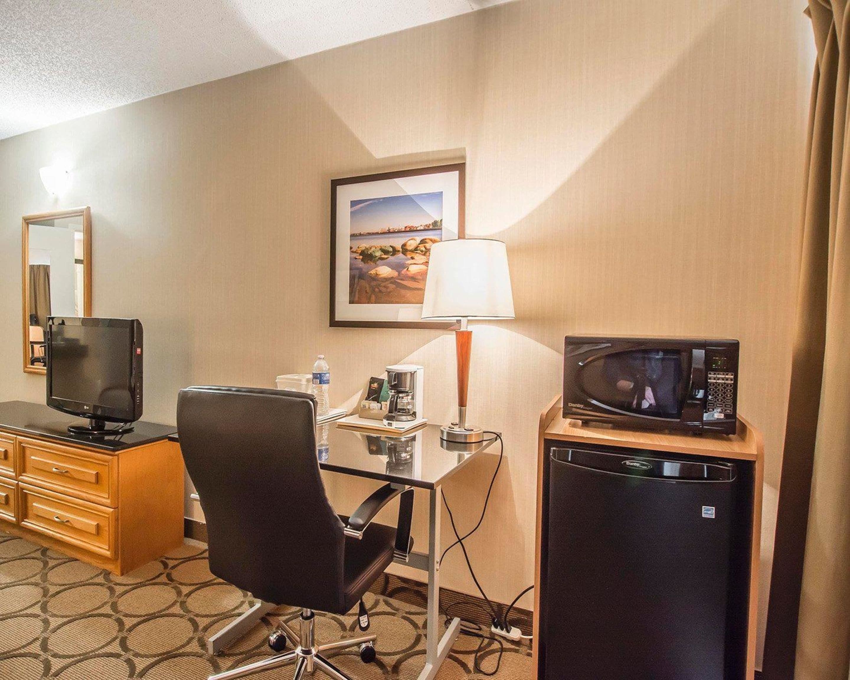 Quarto de hotel com escrivaninha, cadeira, televisão, micro-ondas e pequeno frigorífico.