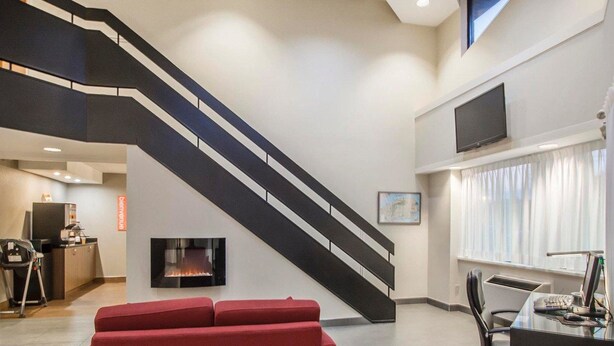 A modern living room with a red sofa, a fireplace, a staircase, and a desk with a computer. - Comfort Inn Rimouski (Rimouski)