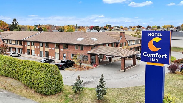 A Comfort Inn hotel with a brick exterior, a covered parking area, and a clear blue sky.