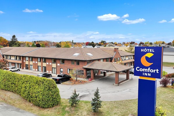 A Comfort Inn hotel with a brick exterior, a covered parking area, and a clear blue sky.