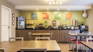 A cafe with wooden tables and chairs, a coffee machine, and a refrigerated display case.
