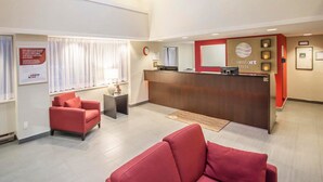 A hotel reception area with a red sofa, a reception desk, and a large window with curtains. - Comfort Inn Rimouski (Rimouski)