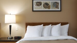 A hotel room with a bed, a nightstand, a lamp, and a framed abstract art piece on the wall.