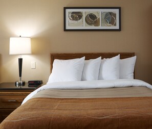 A hotel room with a bed, a nightstand, a lamp, and a framed abstract art piece on the wall.