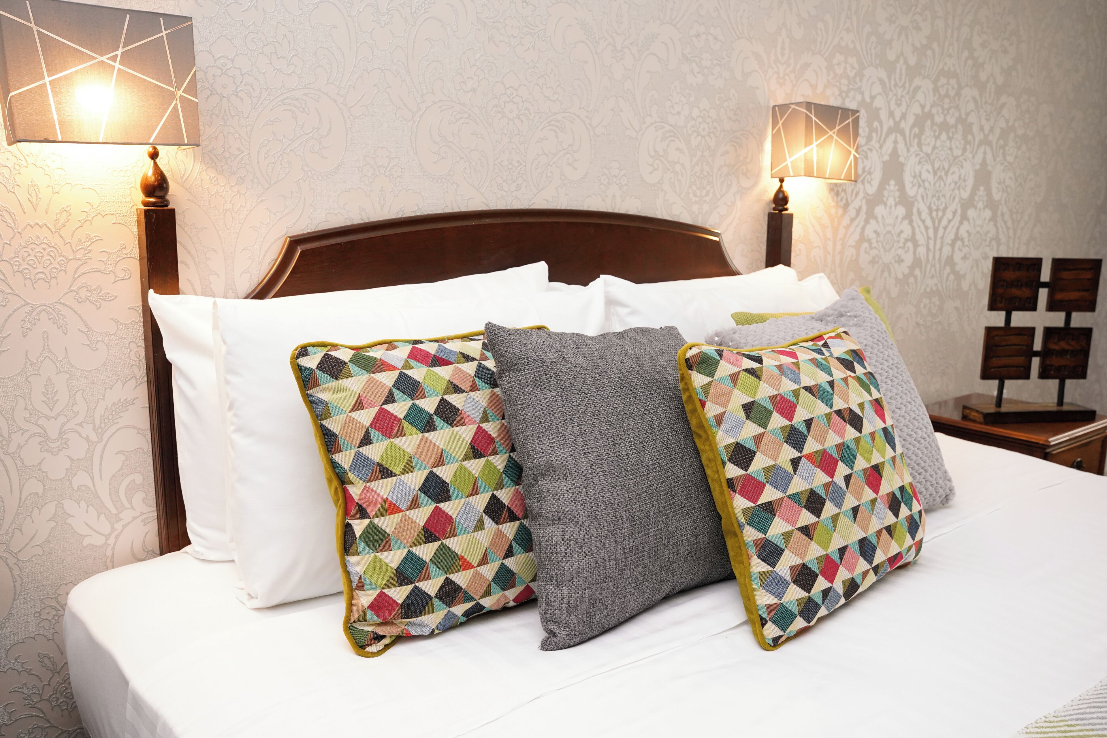 A hotel room with a wooden headboard, white bedding, and two lamps on either side.