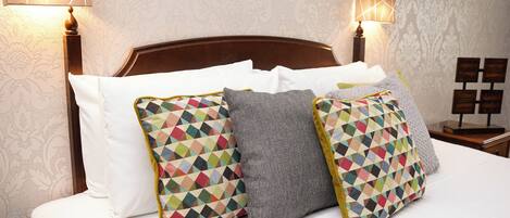 A hotel room with a wooden headboard, white bedding, and two lamps on either side.