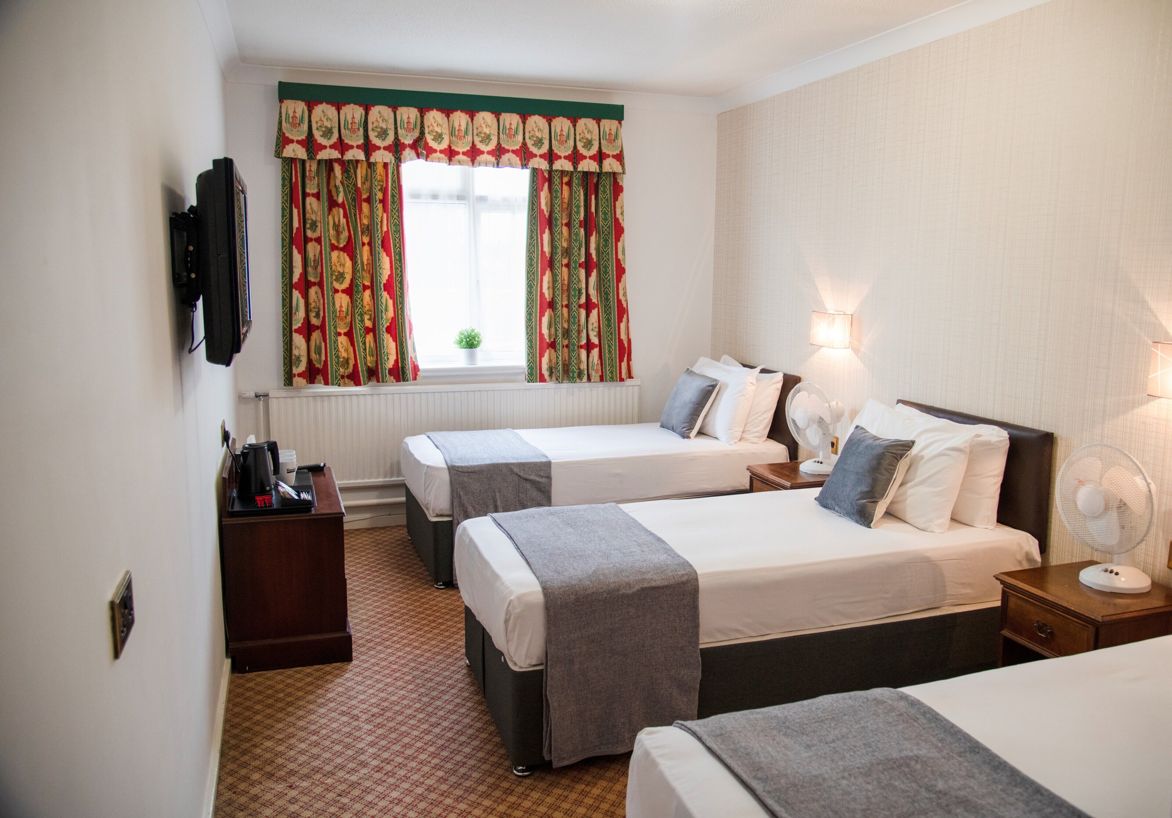 A hotel room with two beds, a desk, a chair, a TV, and a window with curtains.