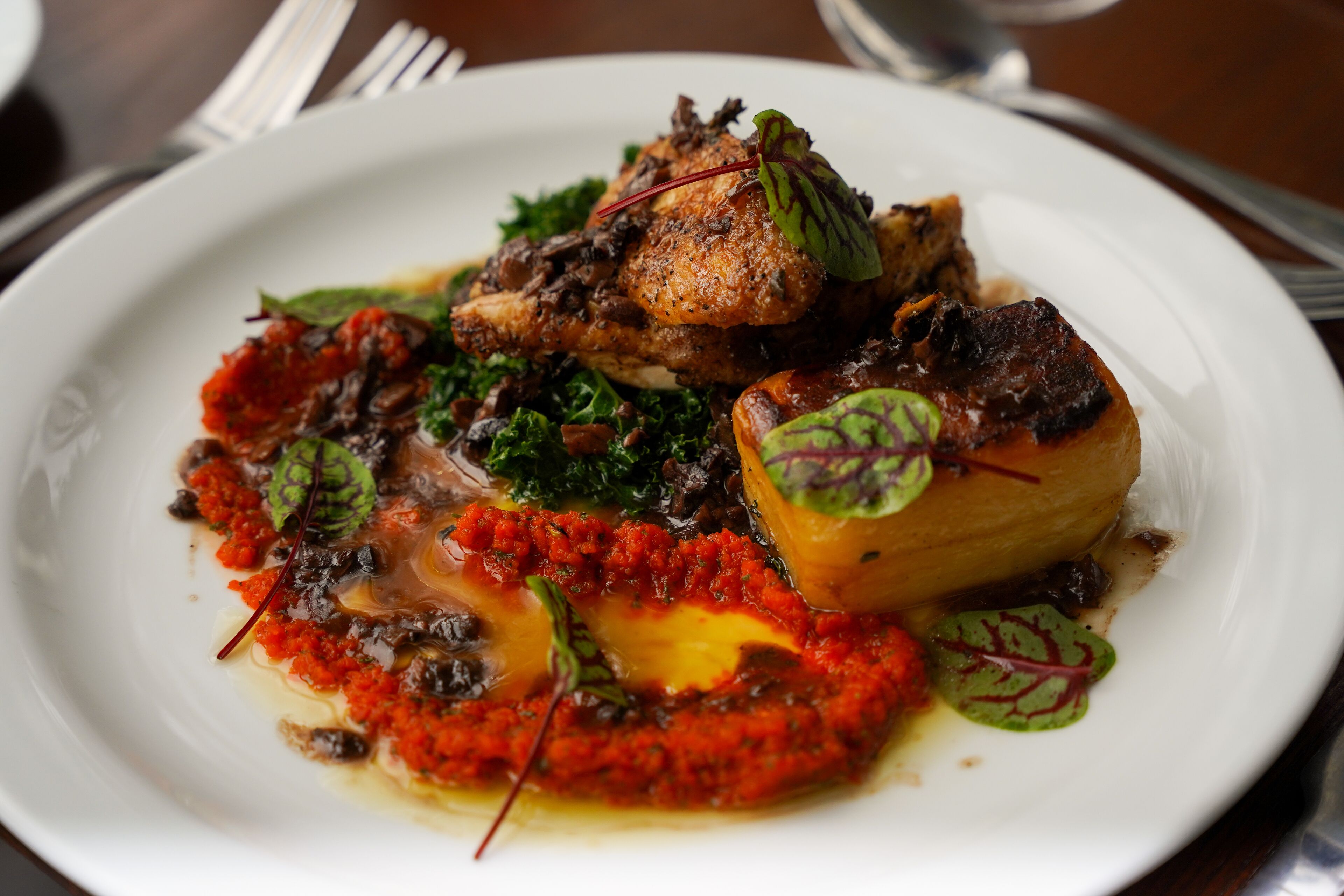 Un plato de comida con diversos platos, incluyendo lo que parece ser un pollo asado, una guarnición de verduras verdes y una salsa roja.