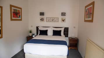 A neatly made bed with a blue blanket, two bedside tables with lamps, and three framed pictures on the wall.