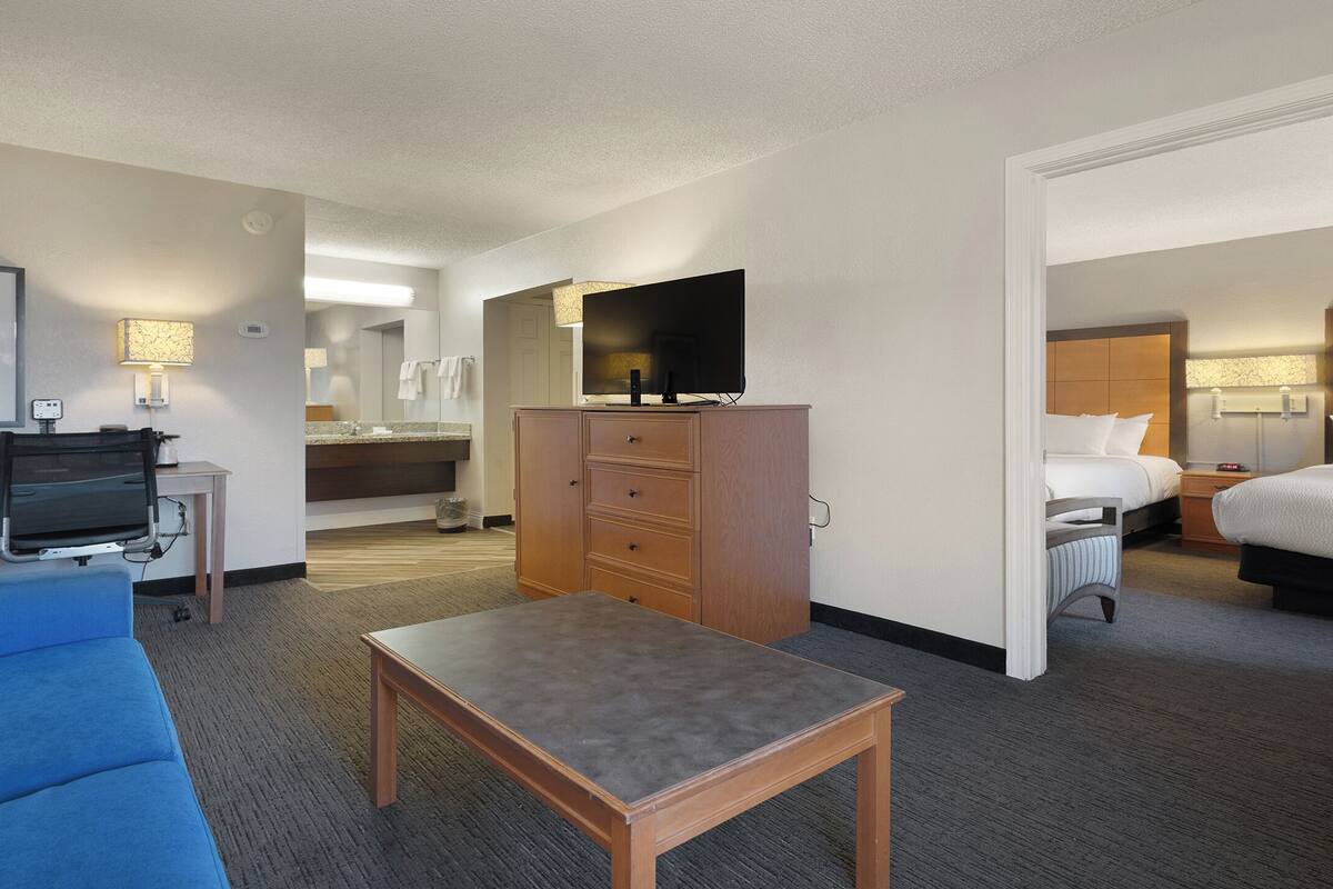 Een hotelkamer met een bed, een bureau, een televisie, een badkamer en uitzicht op de gang.