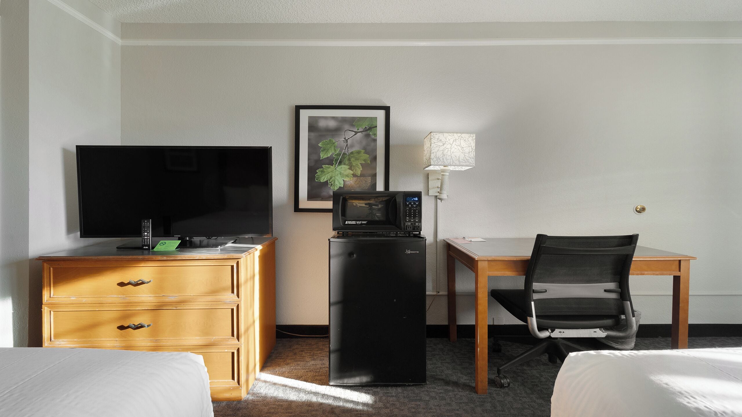 Ein Hotelzimmer mit Fernseher, kleinem Kühlschrank, Schreibtisch und Stuhl sowie einem Bett.